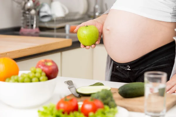 Närbild av gravid kvinna poserar med grönt äpple på kök — Stockfoto