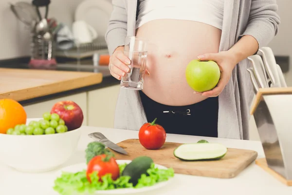 Närbild av gravid kvinna poserar på kök med äpple och glas — Stockfoto