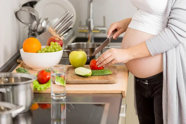 Närbild av gravid kvinna skära grönsaker på träskiva — Stockfoto