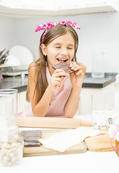 Smiling cute girl biting chocolate bar on kitchen — Stock Photo, Image