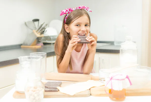 Retrato de niña apoyada en la mesa de la cocina y comiendo chocolate —  Fotos de Stock