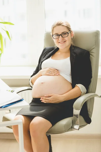 Mulher grávida posando na cadeira no escritório — Fotografia de Stock