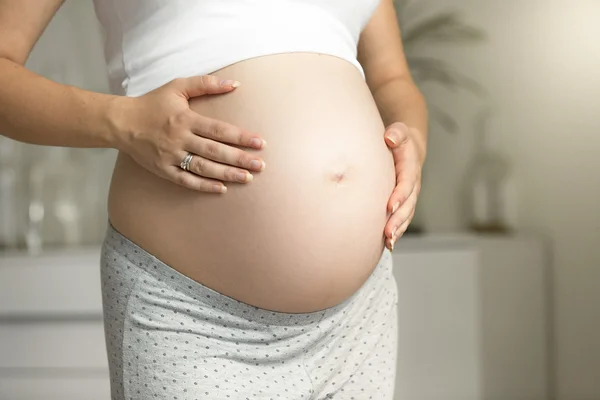 Närbild av gravid kvinna poserar på fönster och hålla händerna på — Stockfoto