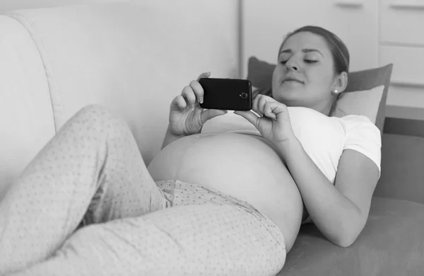 Monochrome shot of pregnant woman typing message on smartphone — Stock Photo, Image