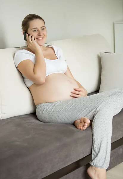 Unga gravid kvinna sitter på soffan och pratar på telefon — Stockfoto