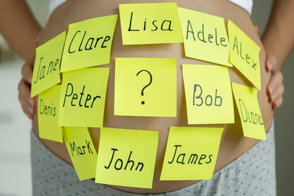 Gros plan de la femme enceinte avec des noms d'enfants sur les autocollants de mémo sur b — Photo