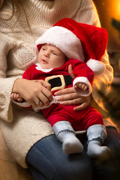 Mãe segurando menino recém-nascido em Santa traje na lareira — Fotografia de Stock