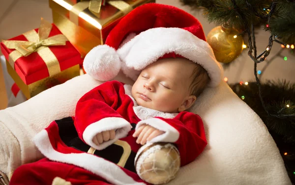 Menino recém-nascido em roupas de Papai Noel deitado sob a árvore de Natal — Fotografia de Stock