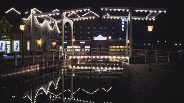 Ponte di legno illuminato che si riflette nel canale — Foto Stock
