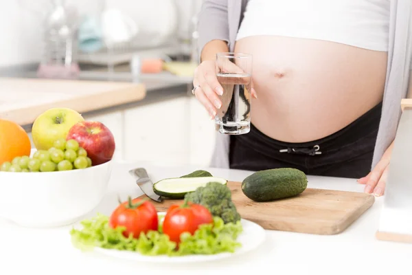 Närbild av gravid kvinna med glas vatten på kök Royaltyfria Stockbilder