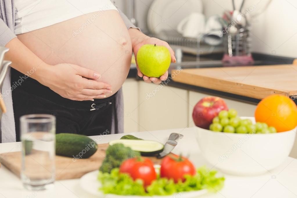 Toned shot of pregnant woman posing with green apple while cooki