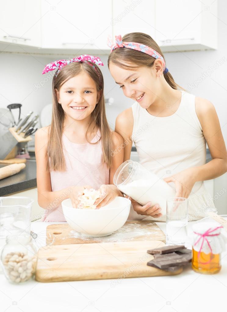 Elder and young sister making dough on kitchen in white bowl