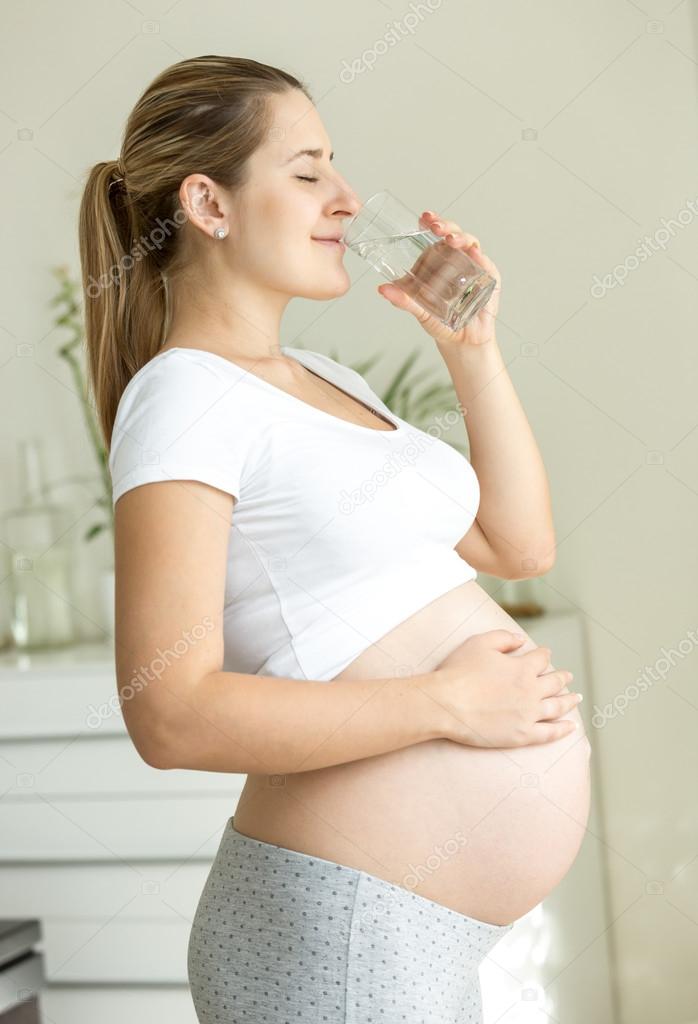beautiful pregnant woman drinking water at living room