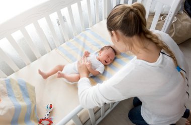 Beşik oturan ve bebeğin elini tutarak anne
