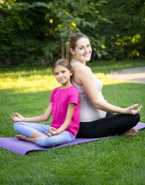 Anne ve gülümseyen kızı pratik yoga ve arka için oturma 
