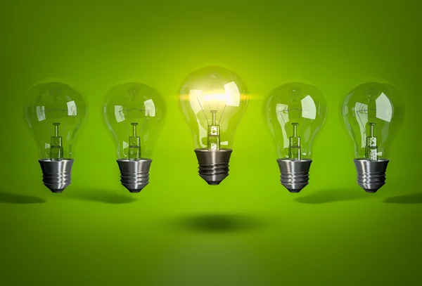 Glowing bulb in row of light bulb on green background — Stock Photo, Image