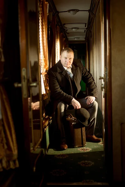 Foto tonificada del hombre en traje vintage sentado en la maleta en tren — Foto de Stock