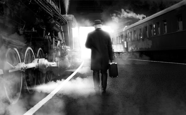 Black and white photo of man in vintage clothes walking on railw