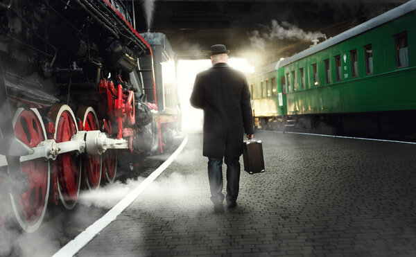 man in bowler hat with suitcase walking on the platform next to 