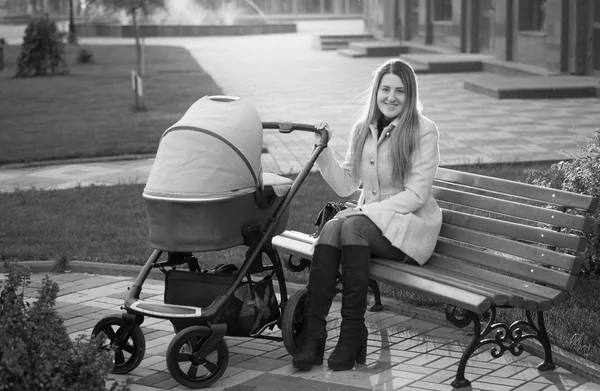 Foto en blanco y negro de la madre sentada en el banco con estrol de bebé —  Fotos de Stock