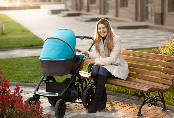 Mamma sitter på bänken och tittar på hennes barn i barnvagn — Stockfoto
