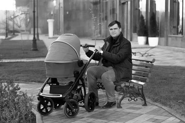 Vader zittend op bankje in park met baby wandelwagen — Stockfoto