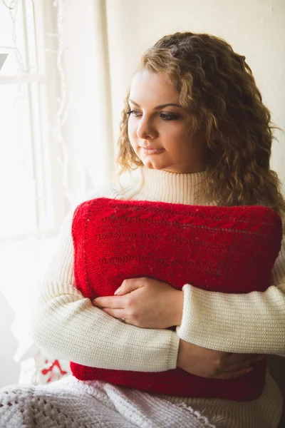 Portrait of beautiful curly woman posing with red cushion at win — Stock Photo, Image