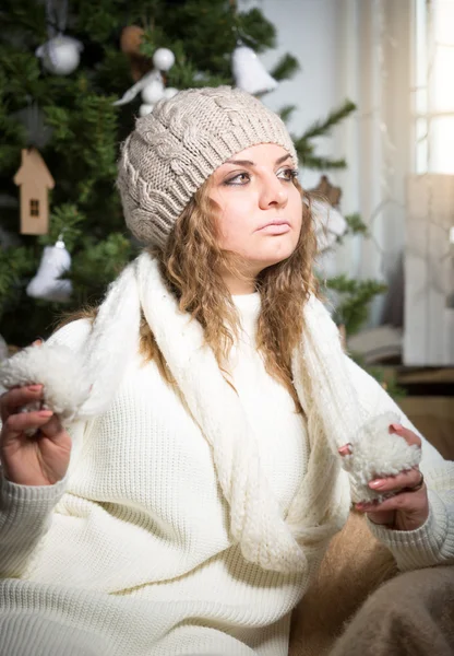 Beautiful curly woman in hat and scarf posing at Christmas tree — Stock Photo, Image