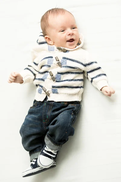 Niño sonriente en jeans y suéter acostado en la cama — Foto de Stock