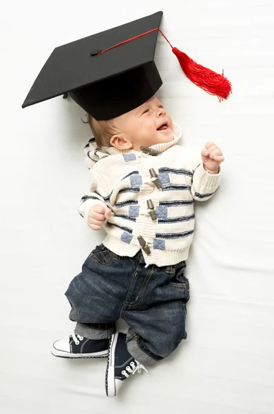 Lindo bebé niño acostado en sombrero de graduación en la cama — Foto de Stock