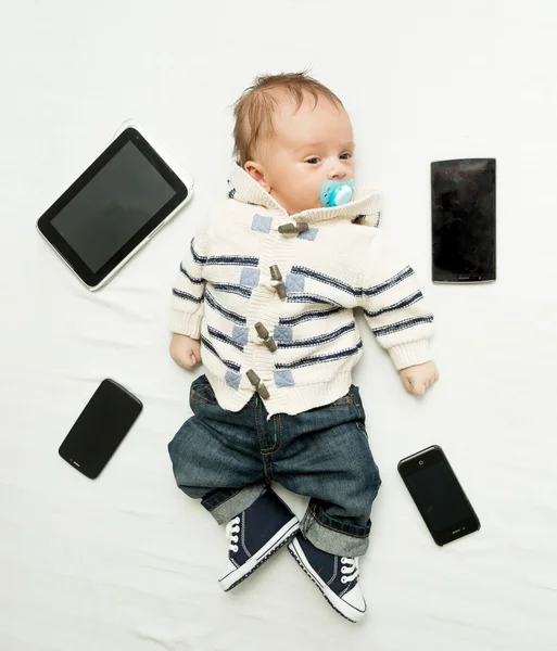 Симпатичний маленький хлопчик лежить на ліжку з цифровими планшетами і смартфонами — стокове фото