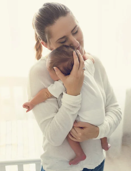 Retrato tonificado de una madre sonriente y cariñosa sosteniendo al bebé en la mano —  Fotos de Stock