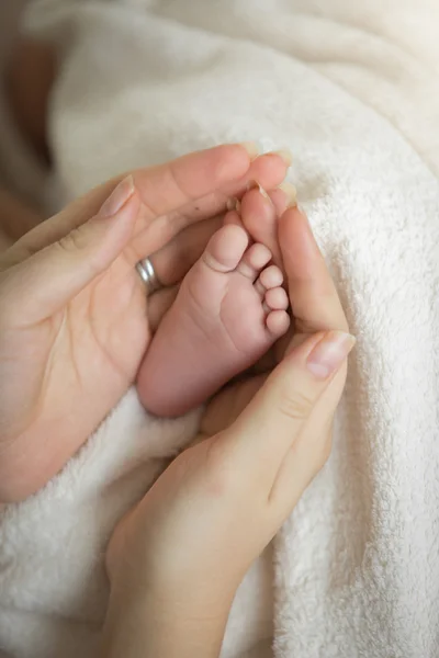 Primer plano de la madre cariñosa sosteniendo los pequeños pies del bebé recién nacido — Foto de Stock