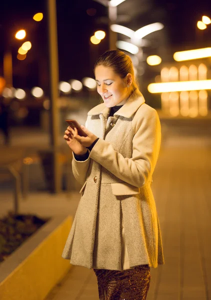 Jovem mulher usando smartphone na rua à noite — Fotografia de Stock