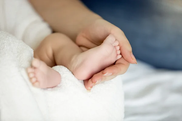 Närbild av mor anläggning nyfödd baby fötter på sängen — Stockfoto