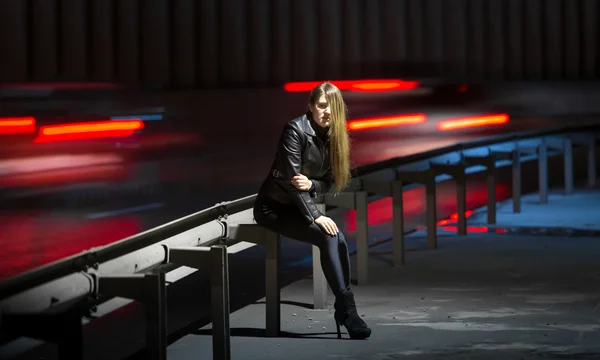 Coches corriendo por delante de la mujer sentada en la carretera por la noche —  Fotos de Stock