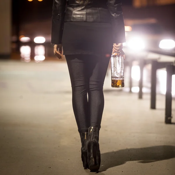 Toned tiro de menina sexy com garrafa andando pela estrada à noite — Fotografia de Stock