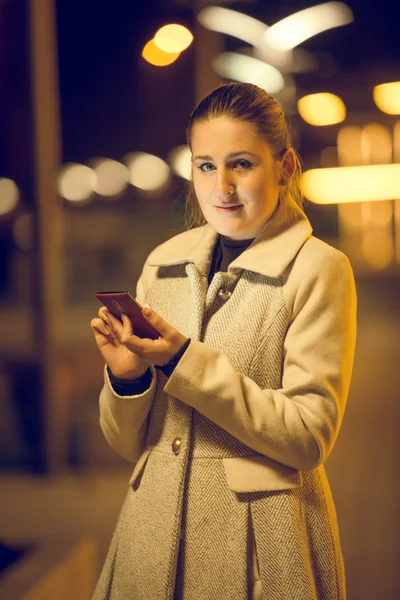 Toned night portrait of young woman using mobile phone on street — Stock Photo, Image