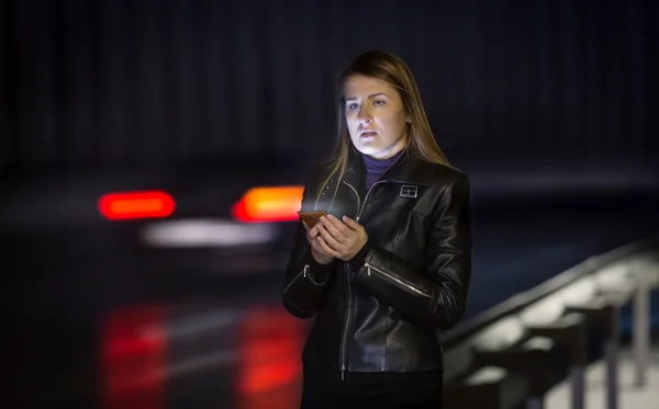 Mujer joven posando en la carretera por la noche con teléfono móvil —  Fotos de Stock