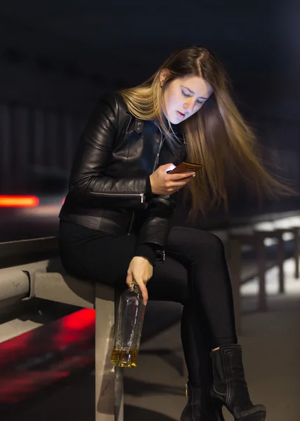 Mujer solitaria sentada en la carretera con whisky y usando ph móvil —  Fotos de Stock