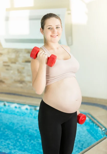 Портрет улыбающейся беременной женщины, поднимающей гантели в спортзале — стоковое фото