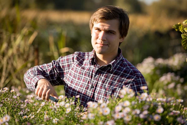 Retrato de hombre joven sonriente poda flores en el jardín — Foto de Stock