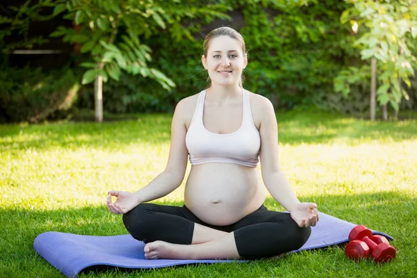 Donna incinta sorridente che pratica yoga sull'erba al parco — Foto Stock