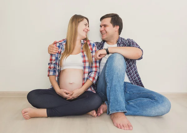 Portret van gelukkige zwangere paar zittend op de vloer en op zoek naar een — Stockfoto