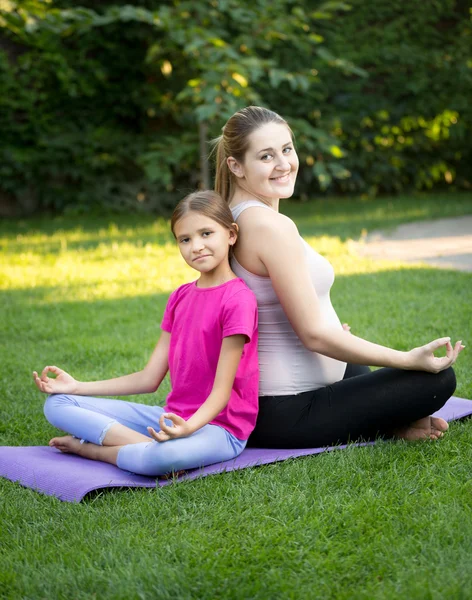 Мать и улыбающаяся дочь практикуют йогу и сидят спиной к — стоковое фото