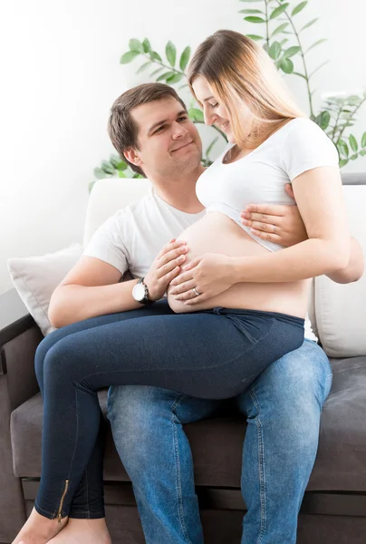 Молодая беременная пара улыбается и смотрит на большой живот — стоковое фото