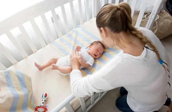 Mother sitting near the cradle and holding baby's hand Royalty Free Stock Photos