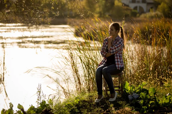 Toned foto de mulher sentada ao pôr do sol junto ao lago — Fotografia de Stock