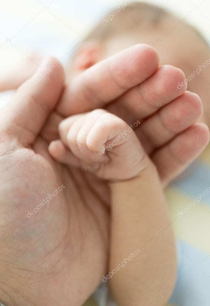 Closeup of father holding newborn baby hand. Image with soft foc