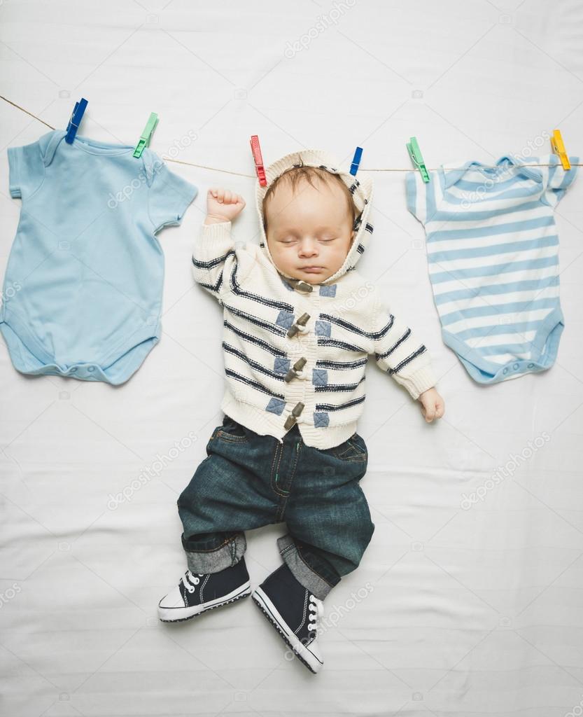 little baby boy in jeans hanging on cord next to drying clothes